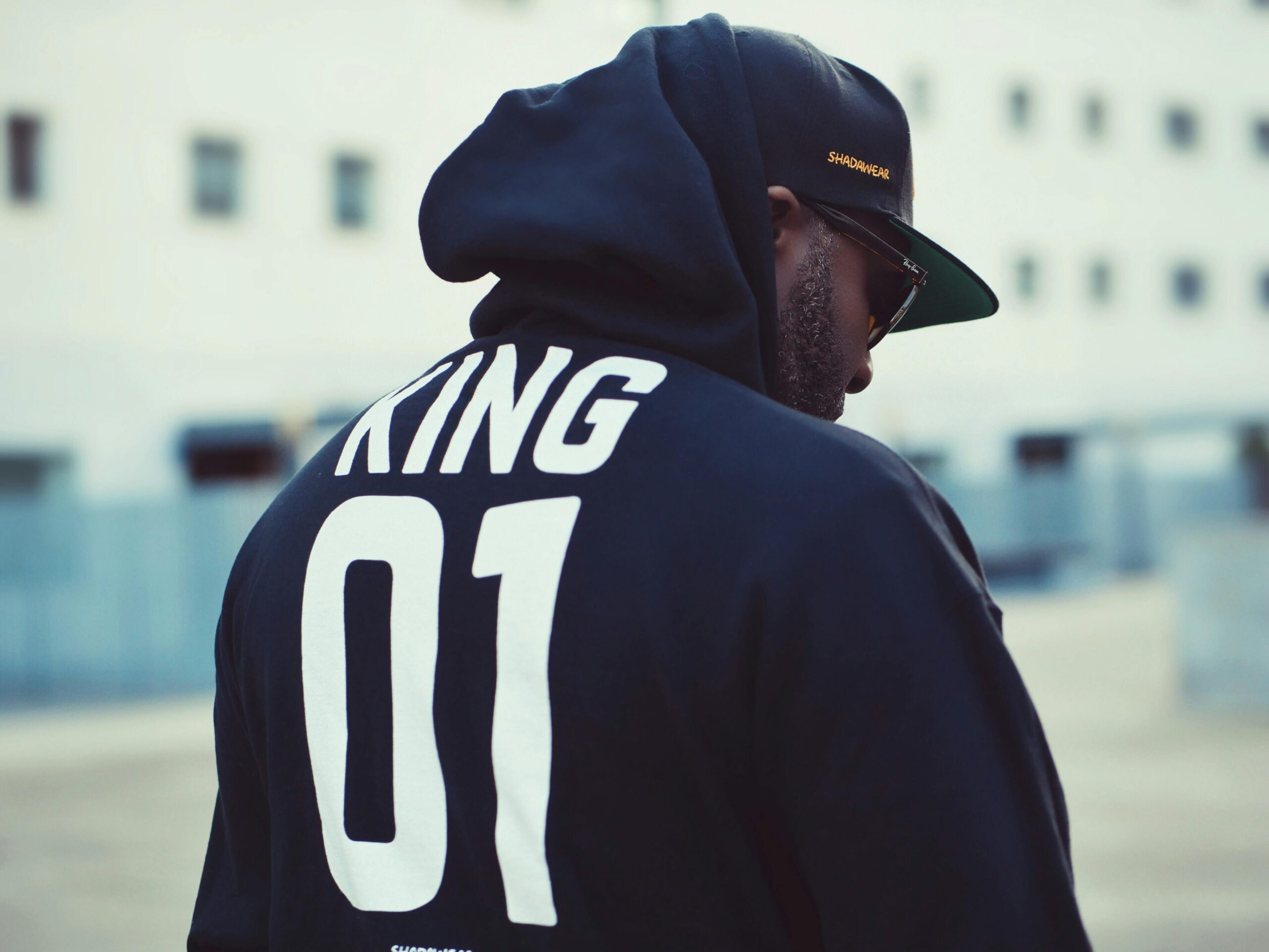 Man in a hoodie and cap with 'KING 01' during daylight in Lisbon.